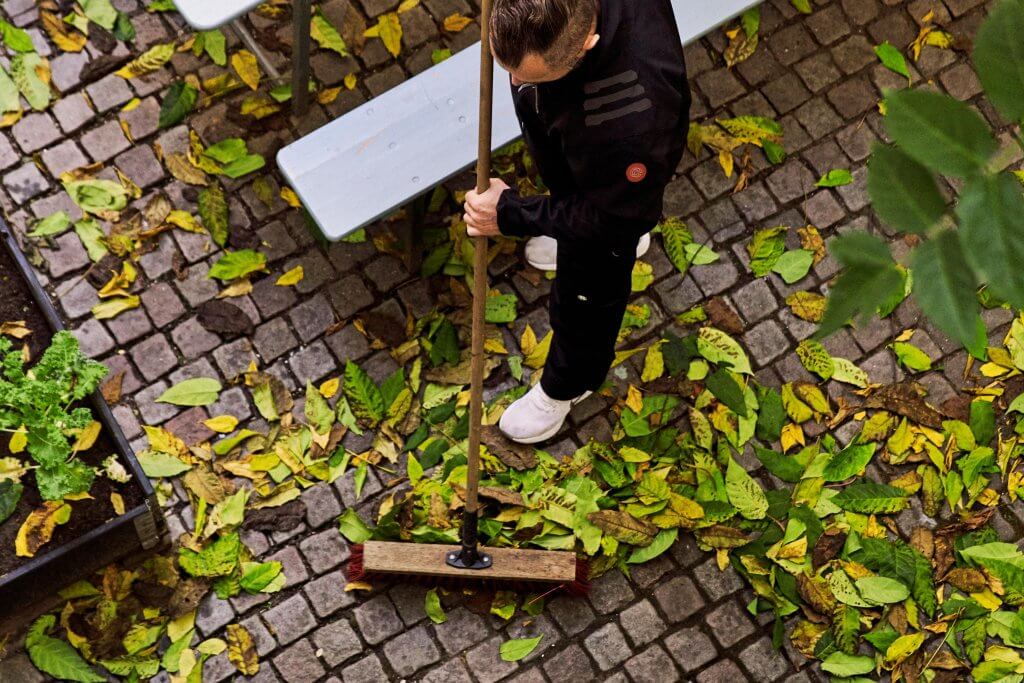 Billede af mand der fejer blade væk med en kost i en privat gård i København.